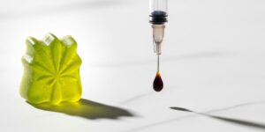 A cannabis gummy edible next to a drop of dark RSO from a syringe, comparing the two products.