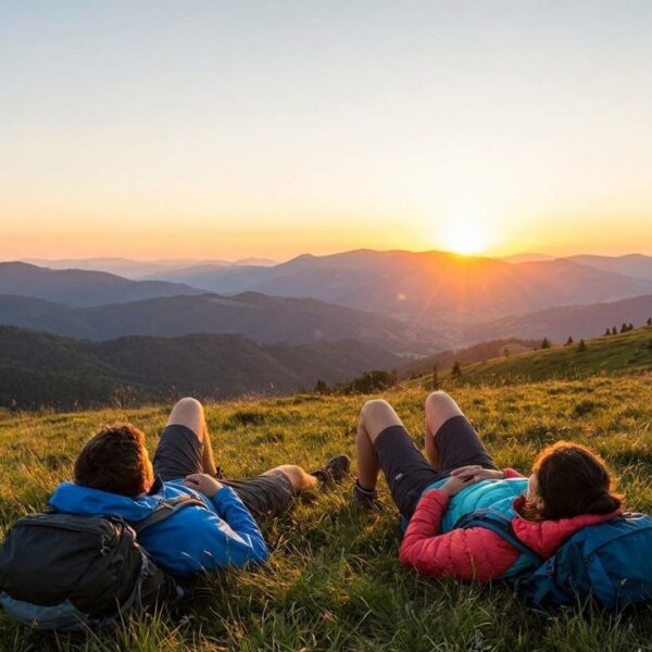 Hikers relaxing on a grassy hill watching sunset over mountains
